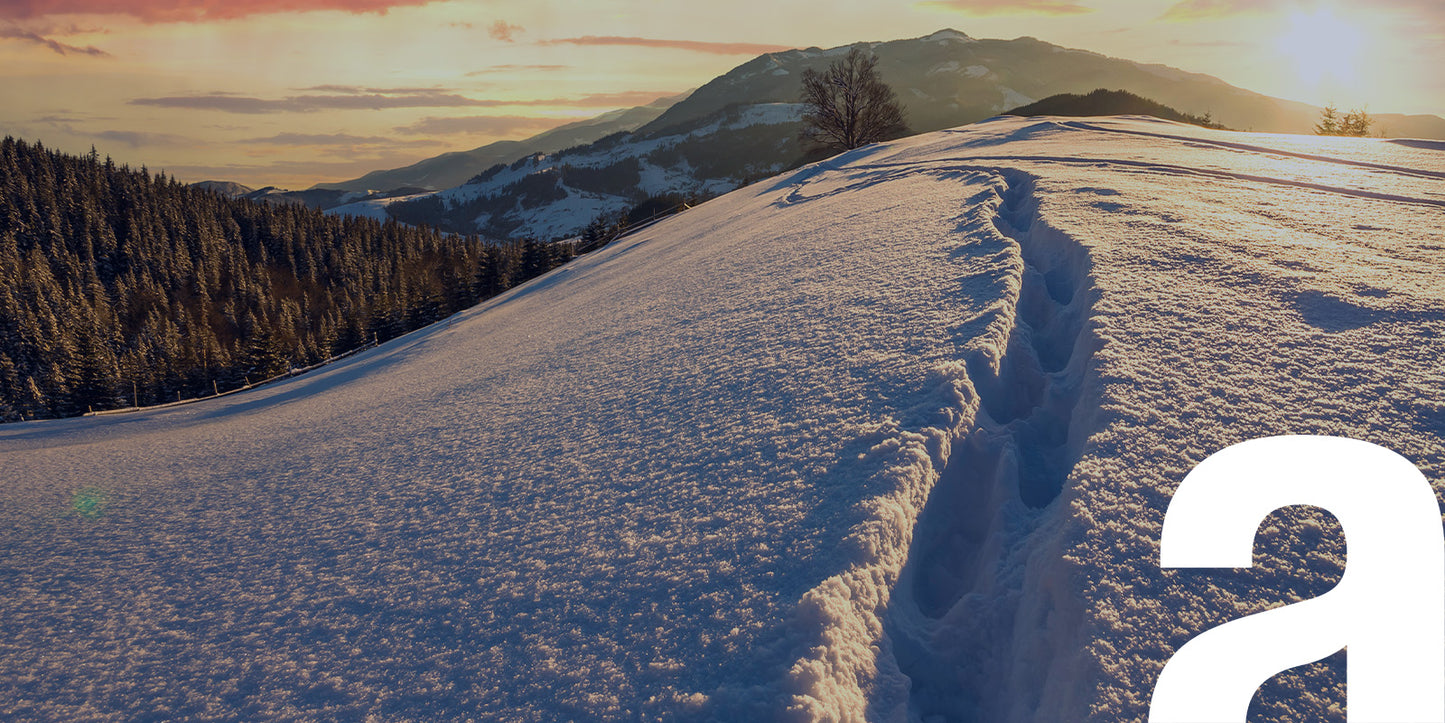 Sentiero innevato tra montagne al tramonto, terreno ideale per le dry bag Atelis a tenuta stagna.